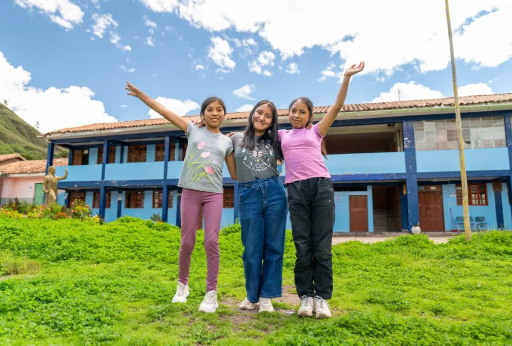 tre piger med armene i vejret foran skole