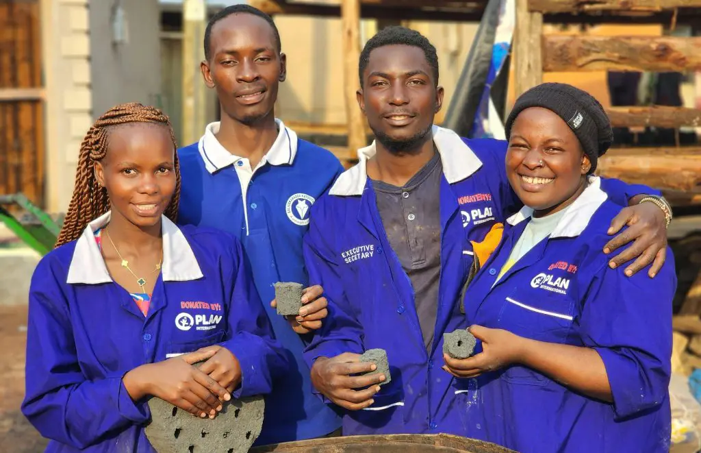 Unge fra Uganda viser deres arbejde frem til kameraet. De laver briketter af kul.